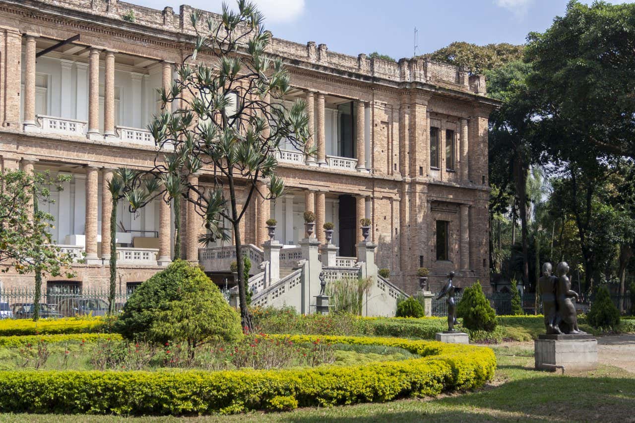 L'imponente facciata della Pinacoteca do Estado immersa nel verde di un giardino con aiuole e statue