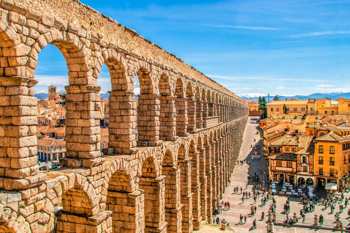 El acueducto de Segovia con sus numerosos arcos divididos en dos pisos junto a los edificios y montañas que rodean el casco histórico de la ciudad