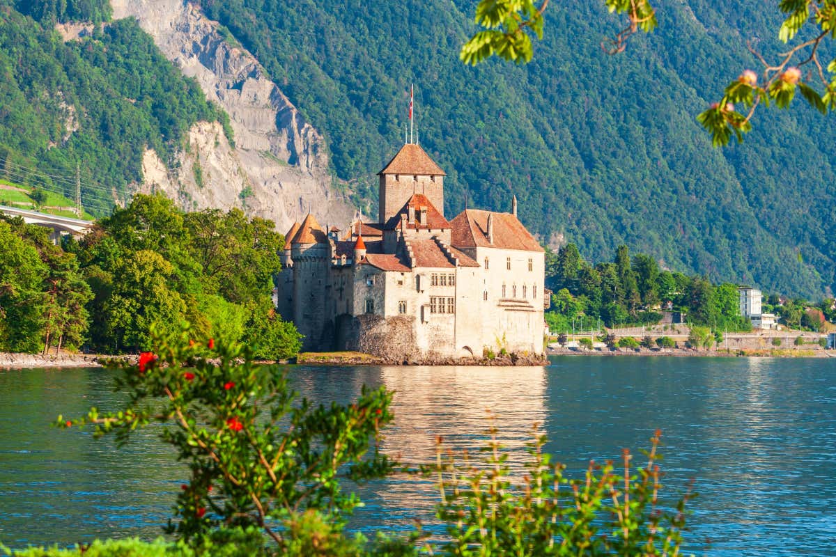 Un castillo medieval con la bandera de Suiza en lo alto situado a orillas de un lago