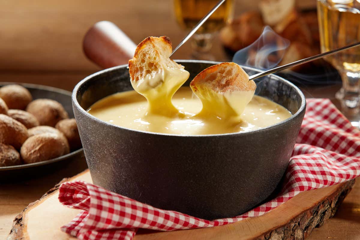 Dos pinchos clavados en dos tostas de pan sobre una olla de fondue de queso suizo