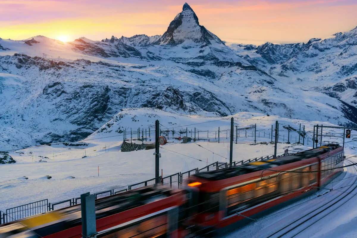 Un tren de color rojo a los pies de unas montañas nevadas