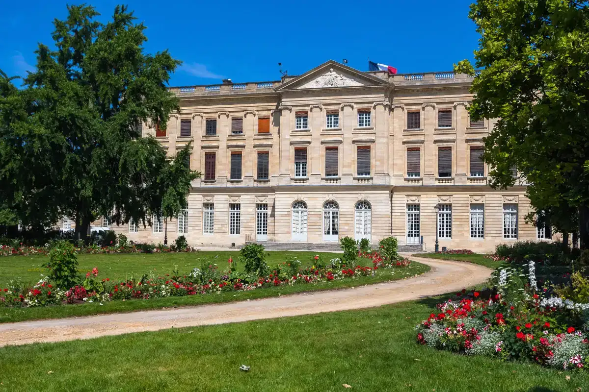 A facade of the Museum of Fine Arts in Bordeaux, a perfectly manicured garden in front with a path lined with red flowers leading up to the entrance