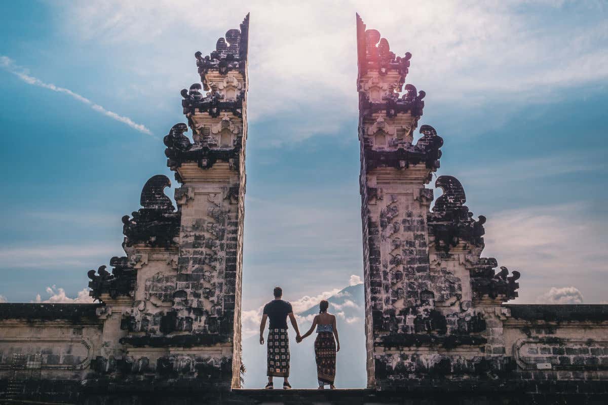Una coppia di spalle tra due enormi colonne di pietra del tempio di Lempuyang a Bali, meta tipica dei viaggi di nozze
