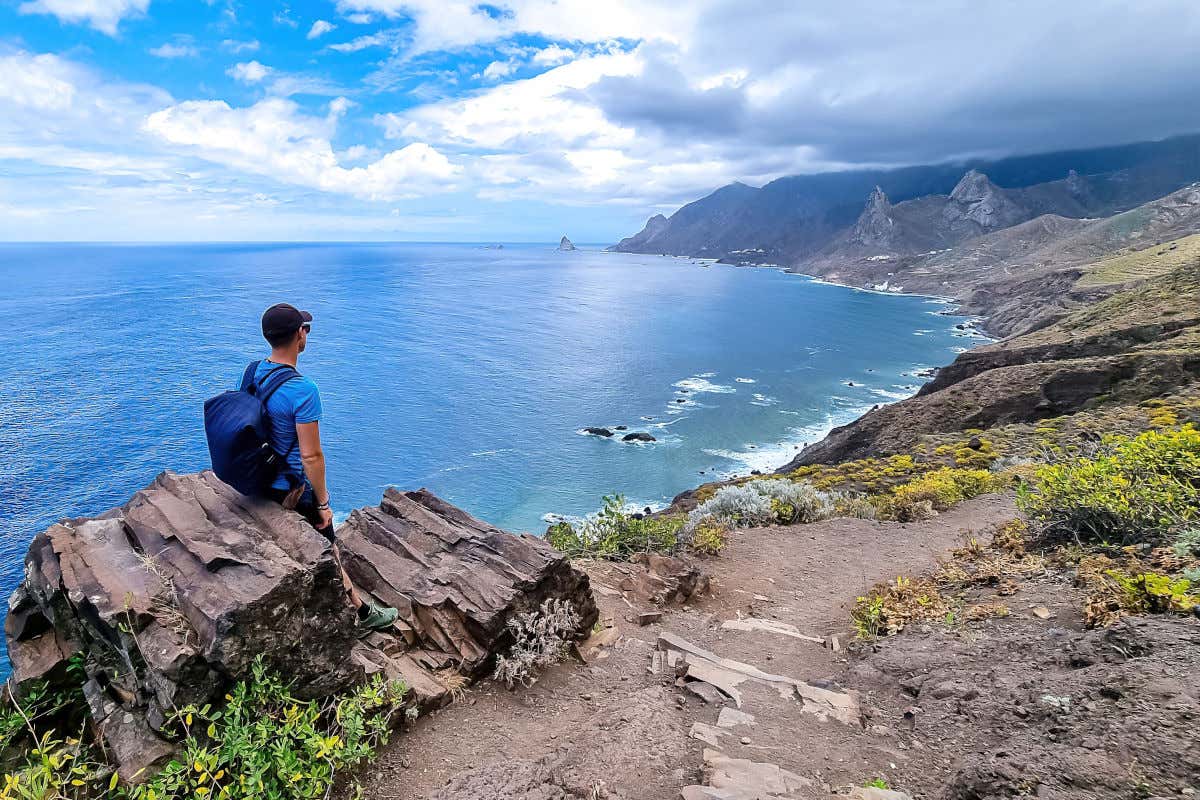 Un hombre sentado en una roca admirando el Atlántico y numerosos acantilados que se extienden por las costas de Tenerife