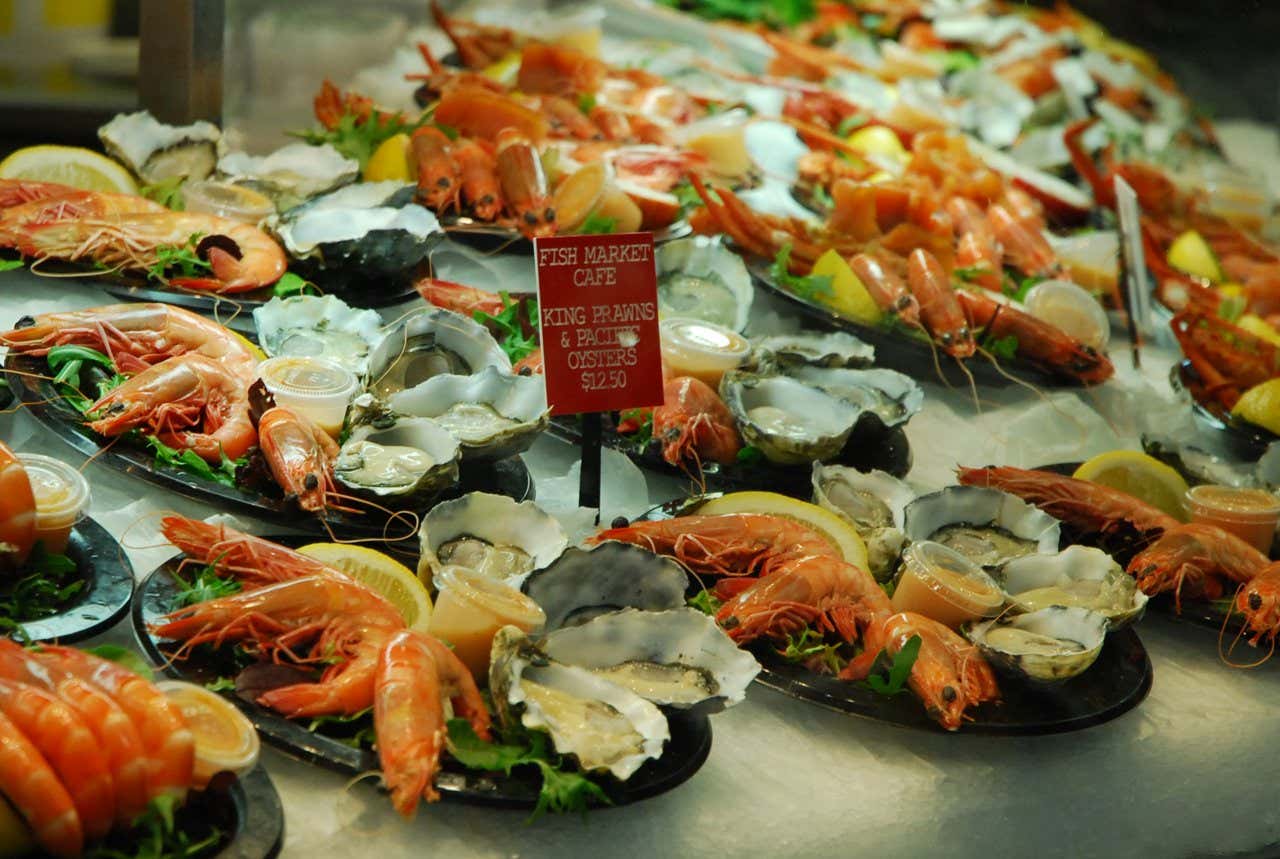 A selection of oysters and prawns with lemon slices on a white surface, with a red sign in the middle