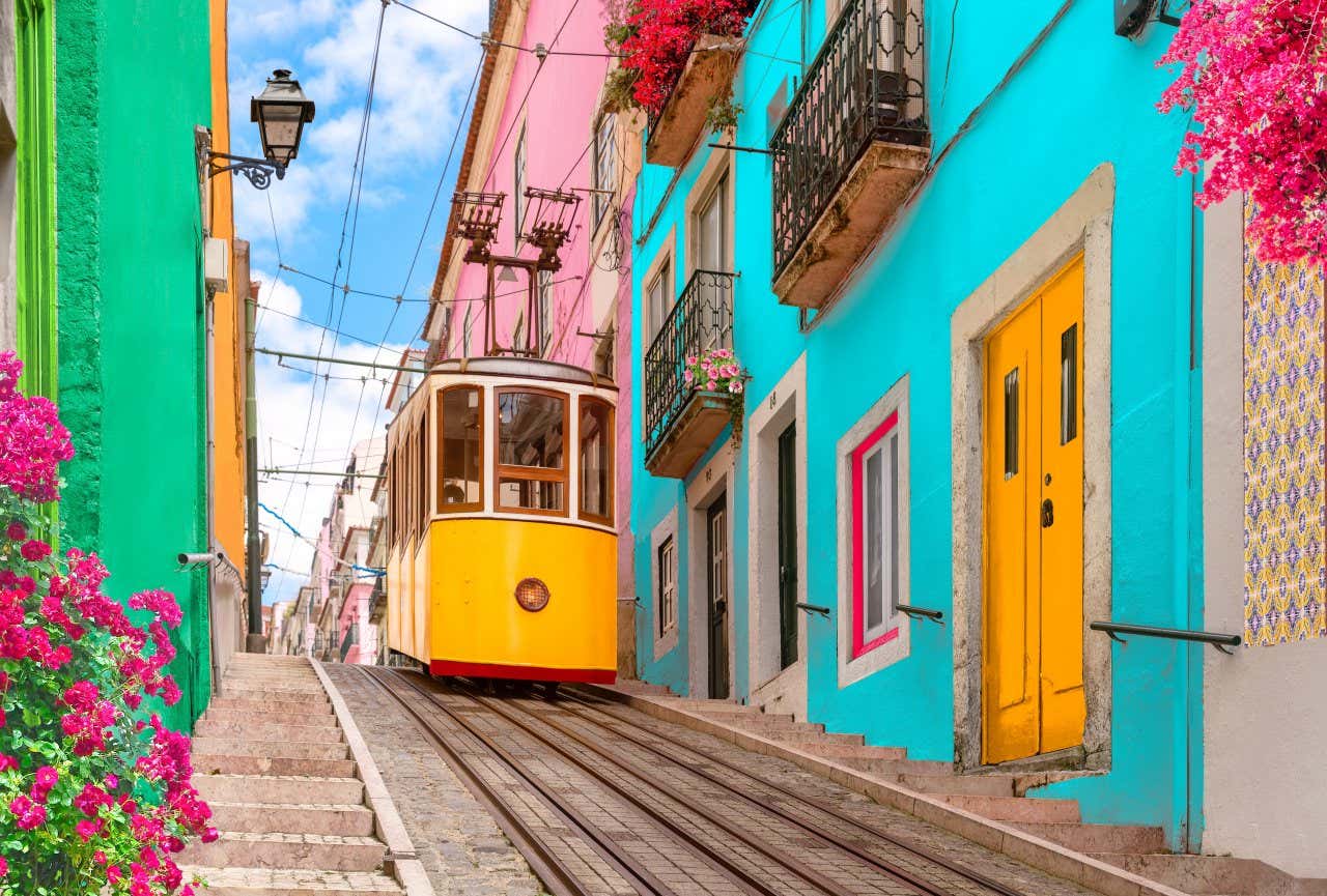 A vintage tramway on a colorful Lisbon street lined with vibrant houses and bright pink flowers