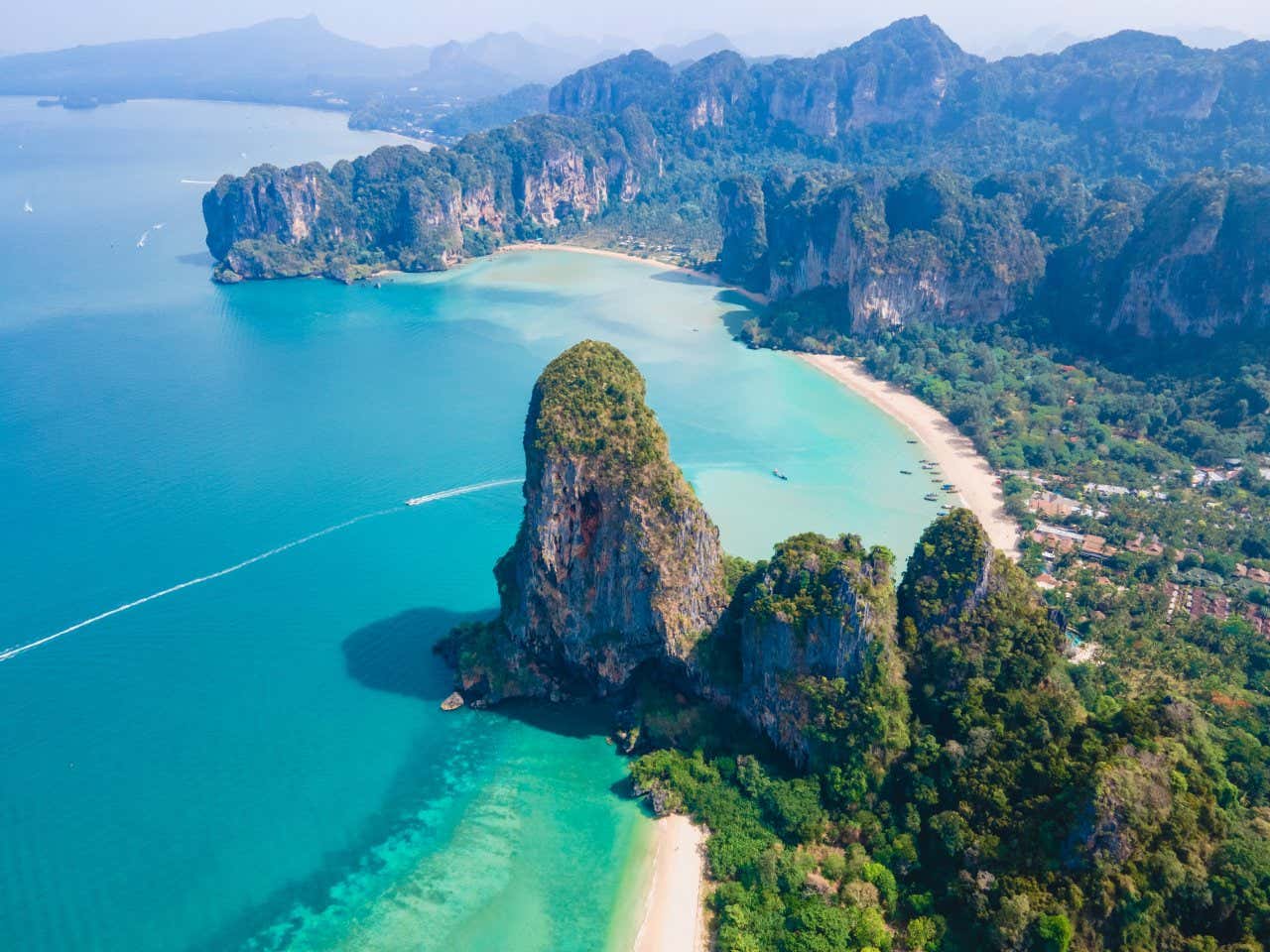 An aerial view of beaches in Phuket, with large cliffs dividing them, and a boat sailing in the water.