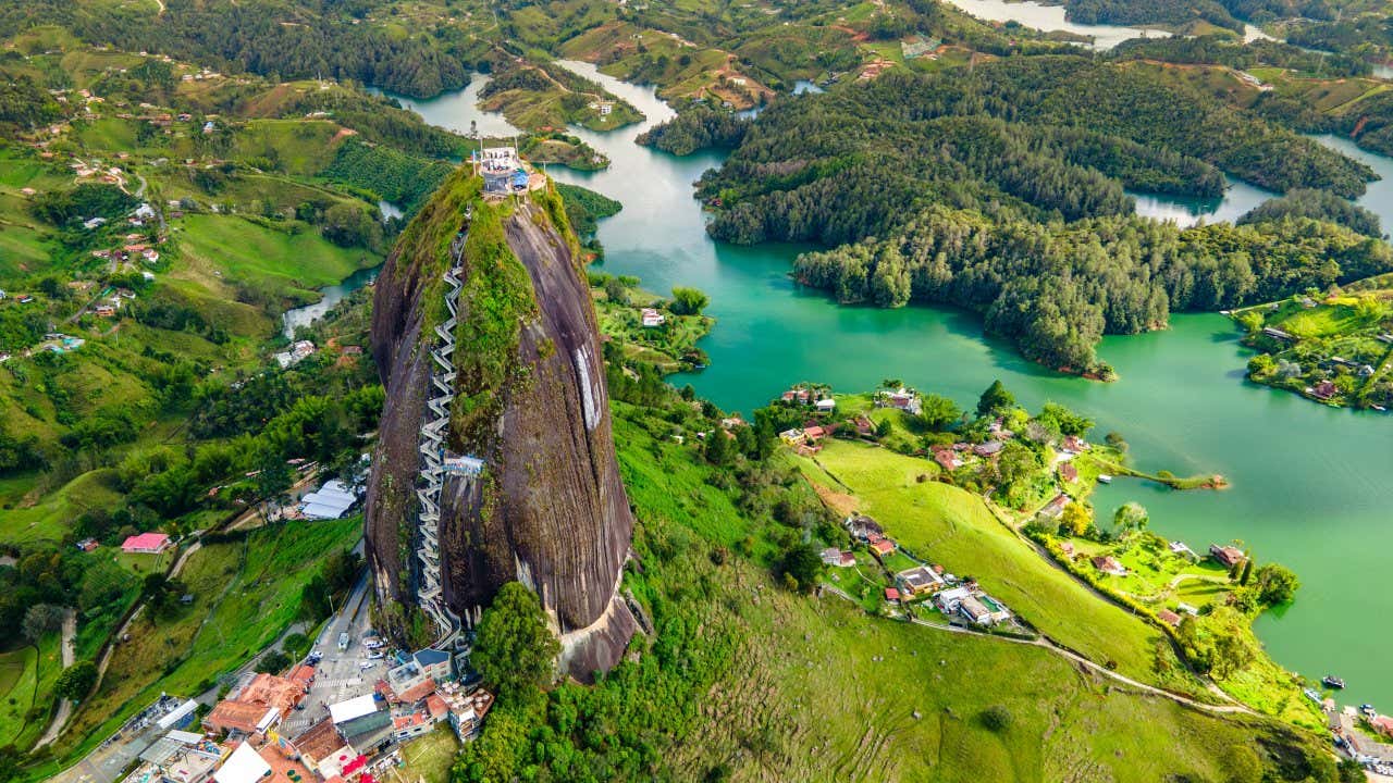 An aerial view of El Peñón de Guatapé in Guatapé, with green vegtation surrounding it in view, and various houses.