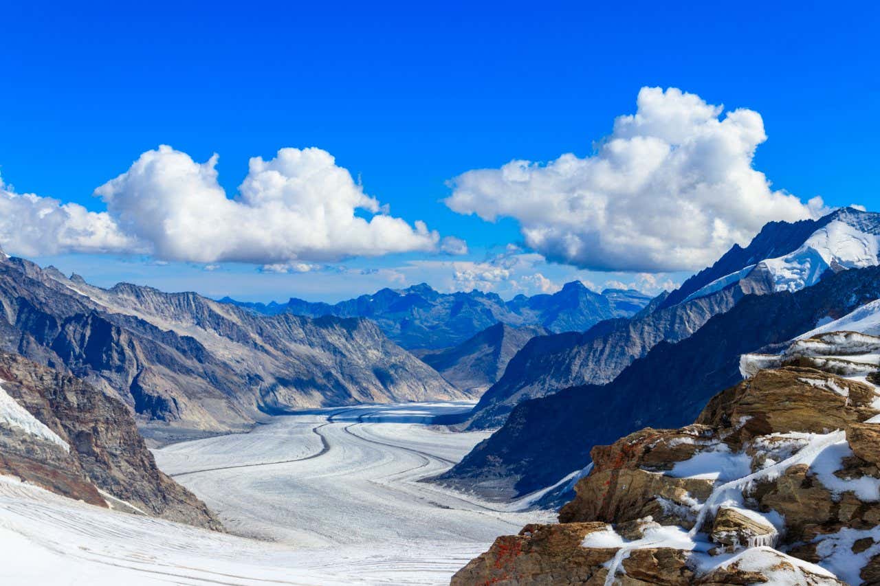 Una vallata coperta di neve fra alte montagne e rocce innevate in primo piano in una giornata con poche nuvole