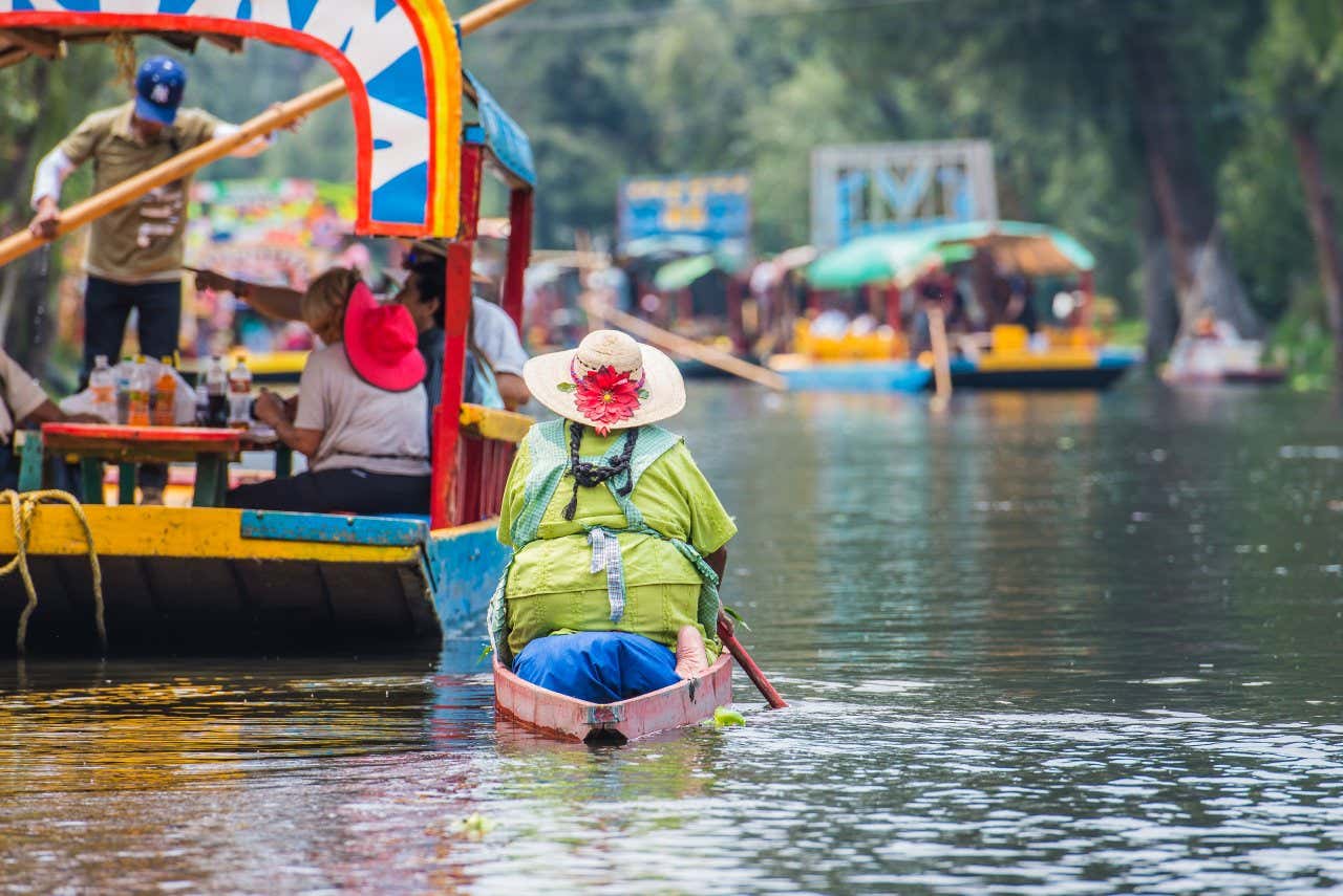 Xochimilco canal with people sailing down it on colourful boats.