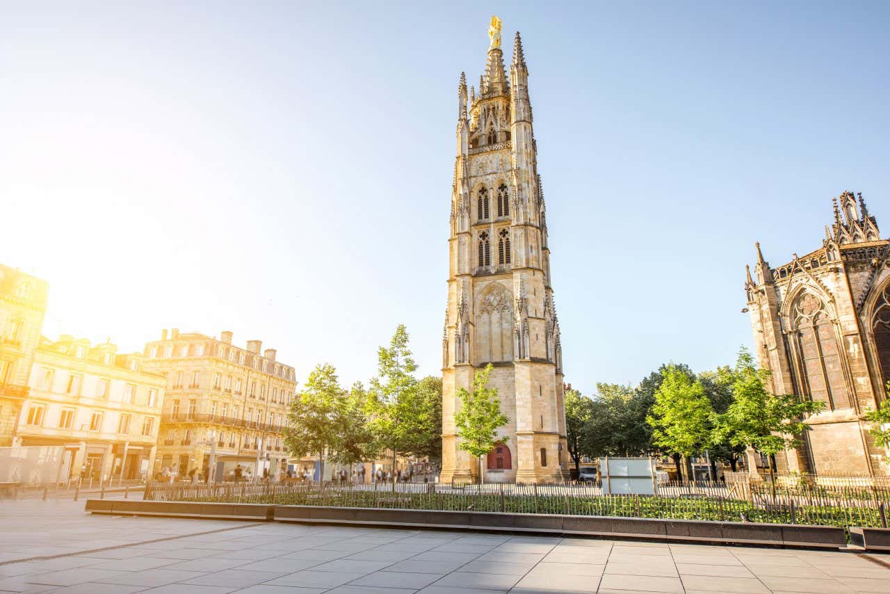 Pey-Berland Tower in the middle of an empty square with no people, the sun shining into frame, the steeple seen from the ground