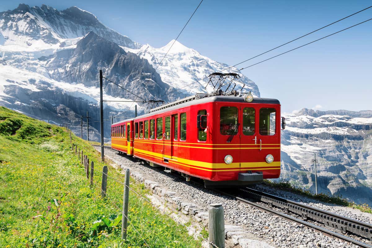 Un tren cremallera de color rojo y amarillo recorriendo un paisaje alpino entre montañas