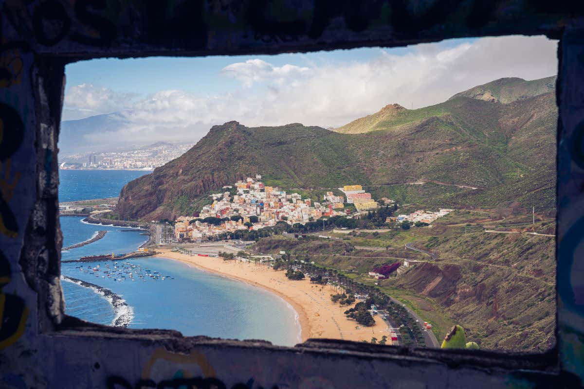 Una ventana de piedra con vistas a una playa de arena dorada y numerosas montañas de Tenerife