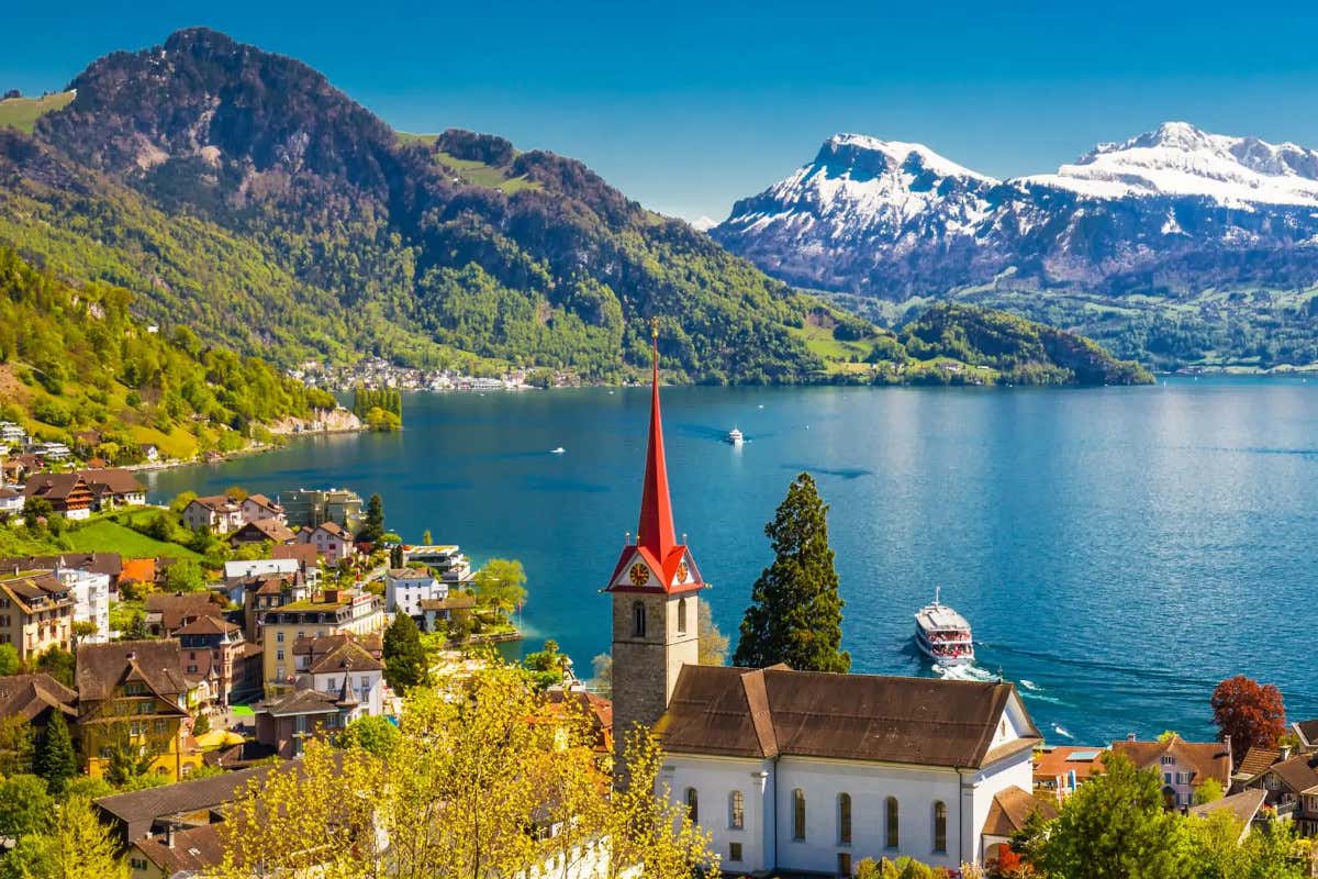 Paisajes de un lago rodeado de montañas, con una iglesia con campanario rojo en primer término