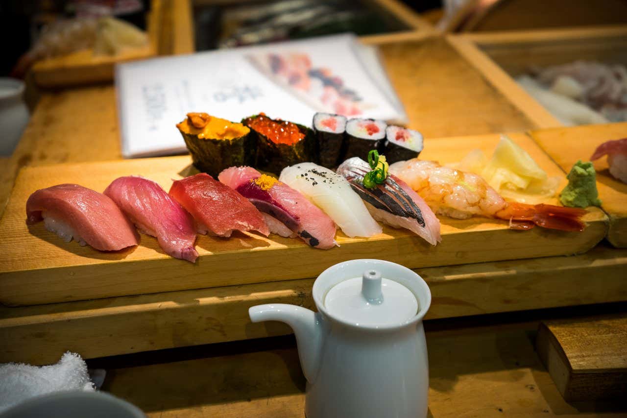 Diversi tipi di sushi e maki a base di pesce serviti su un bancone in legno al mercato ittico di Tsukiji a Tokyo