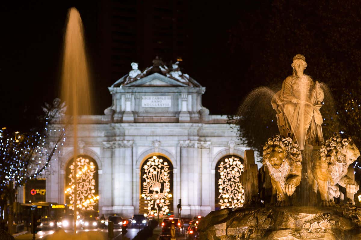 La escultura de Cibeles iluminada por la noche frente a la Puerta de Alcalá decorada con luces de Navidad