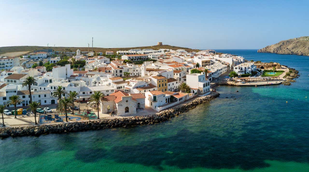 A view of the coast of Fornells in Menorca, with a cloudy sky in the background.