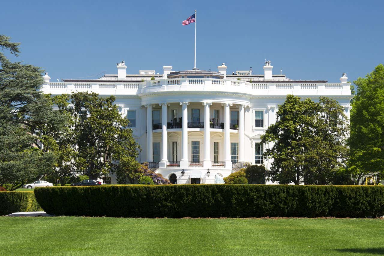 The White House in Washington, DC, with an extensive yard and groomed bushes out front at sunset