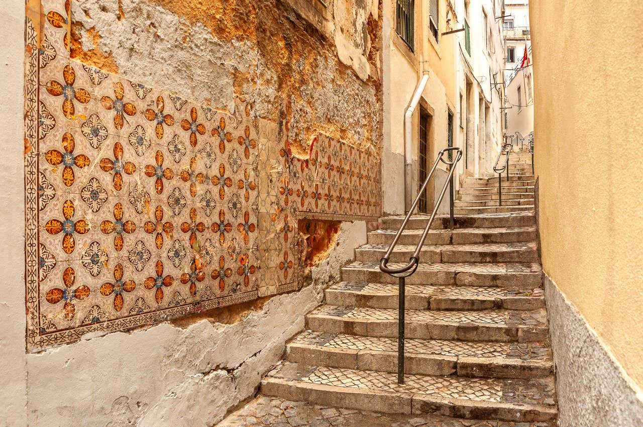 A narrow street in Alfama with steps and handrails going into the distance, and buildings with yellow and orange walls.