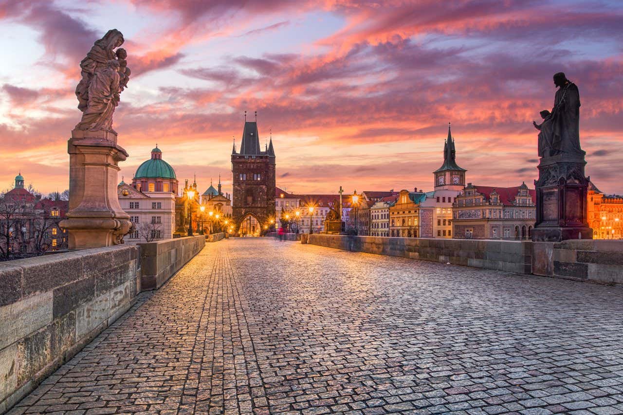 The Charles Bridge in Prague, with statues and street lamps lining either side, and a red cloudy sky above.