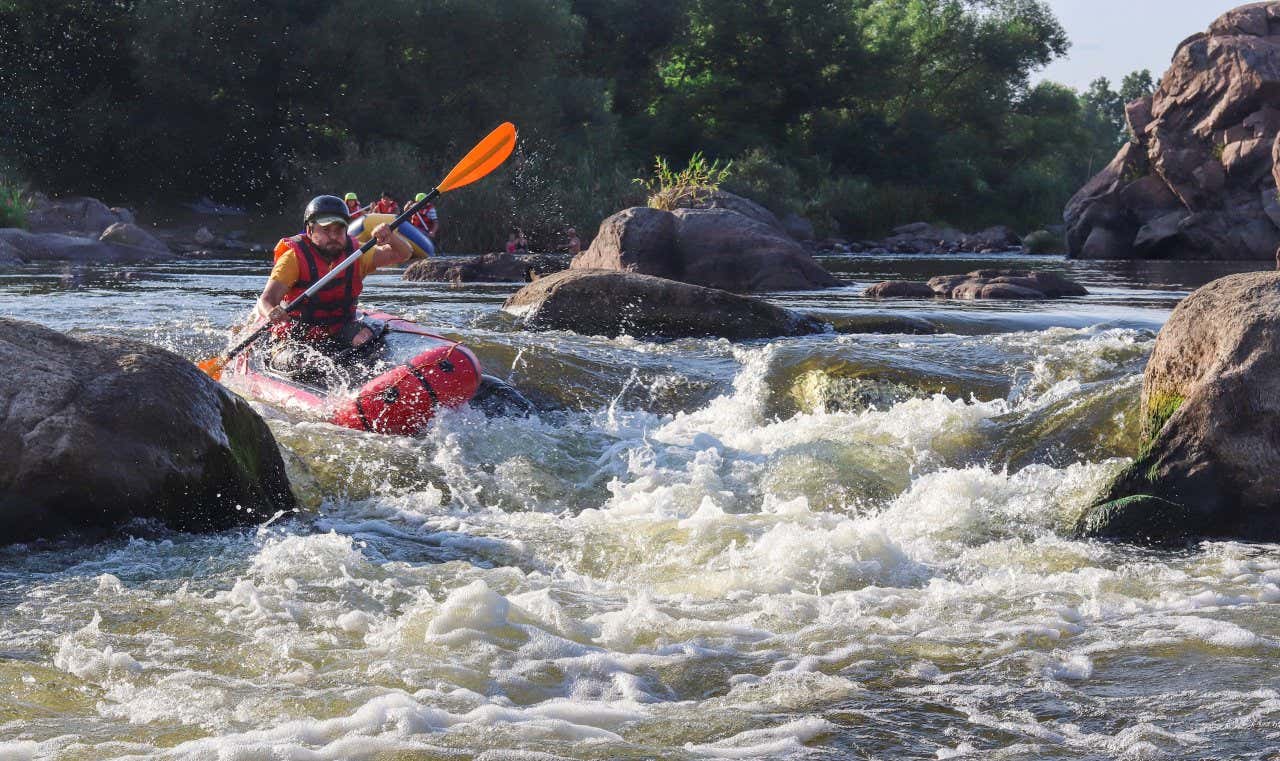 A man in a red life jacket and a black helmet river rafting in a red boat down the Chili River in Arequipa.