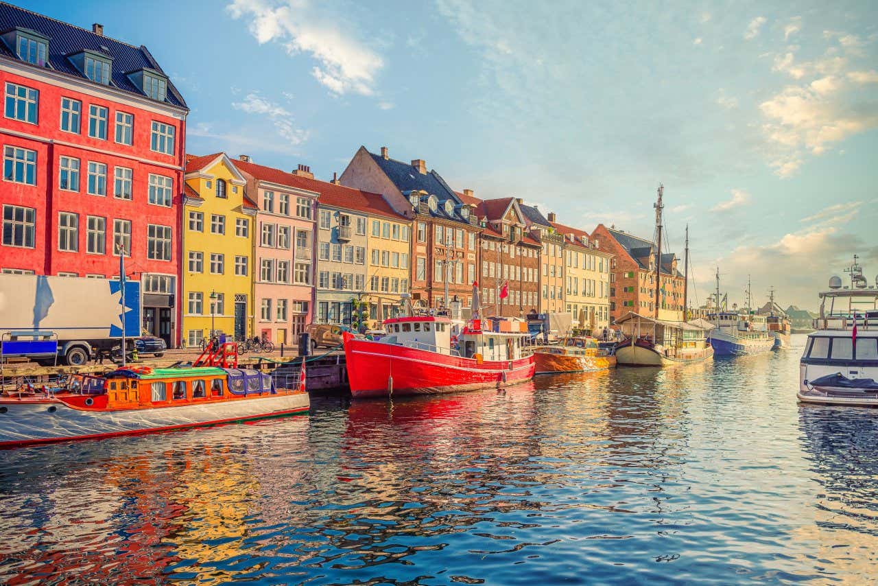 Boats lining the canals of Copenhagen, with colourful buildings in the background and cloudy skies.