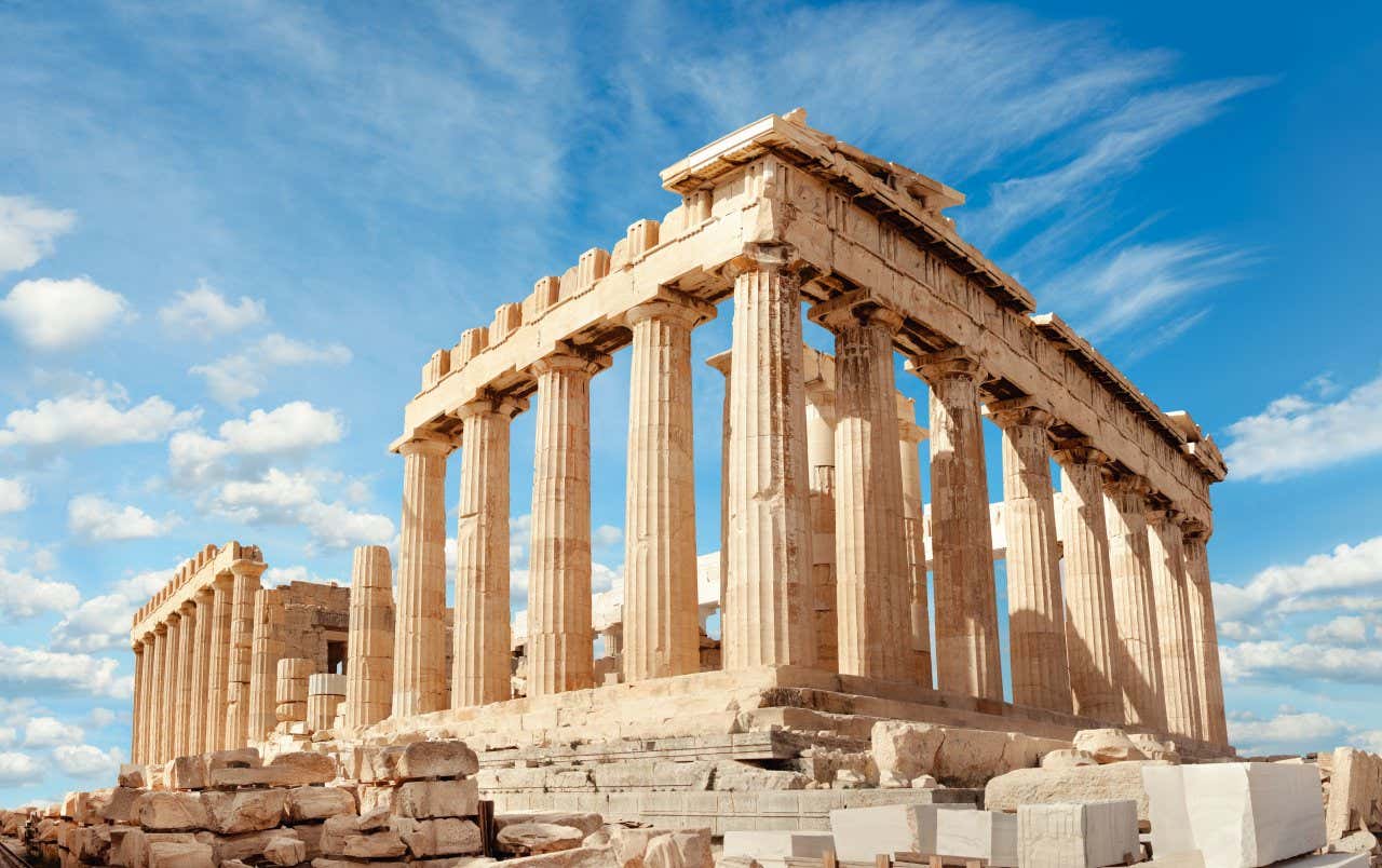 A side view of the Parthenon in Athens with a vaguely cloudy sky in the background.