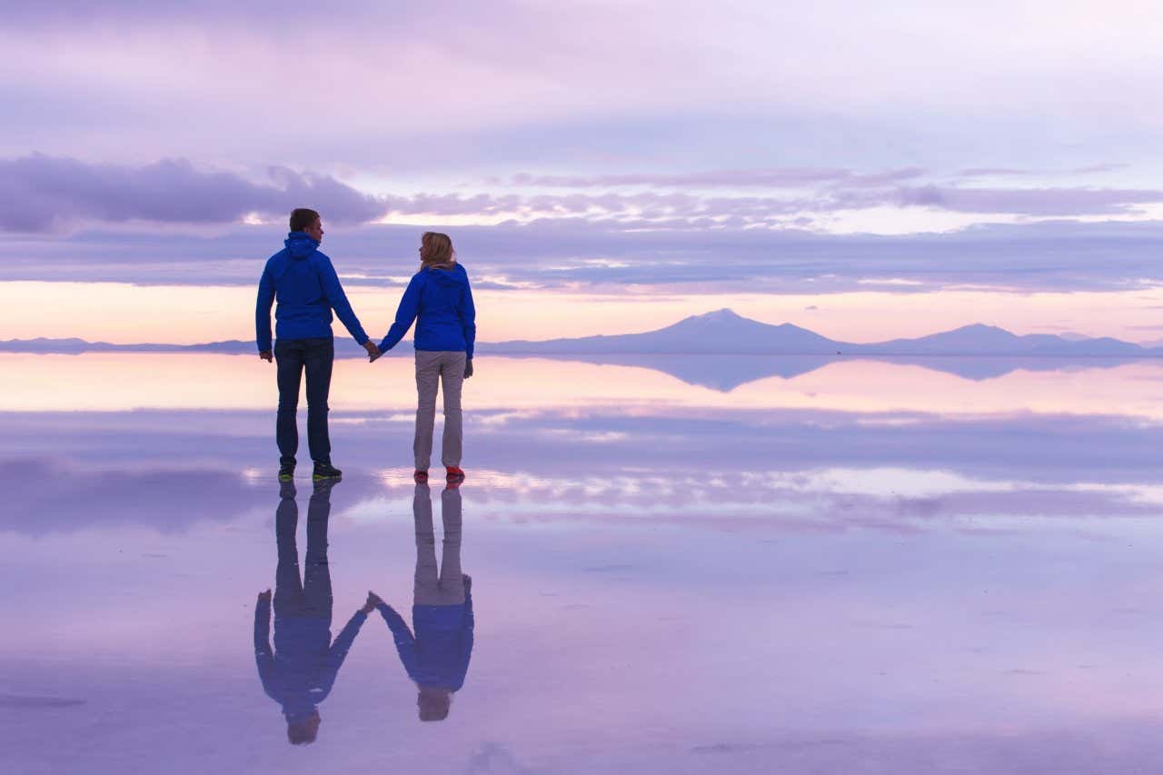 Casal e seu reflexo de mãos dadas no salar de Uyuni