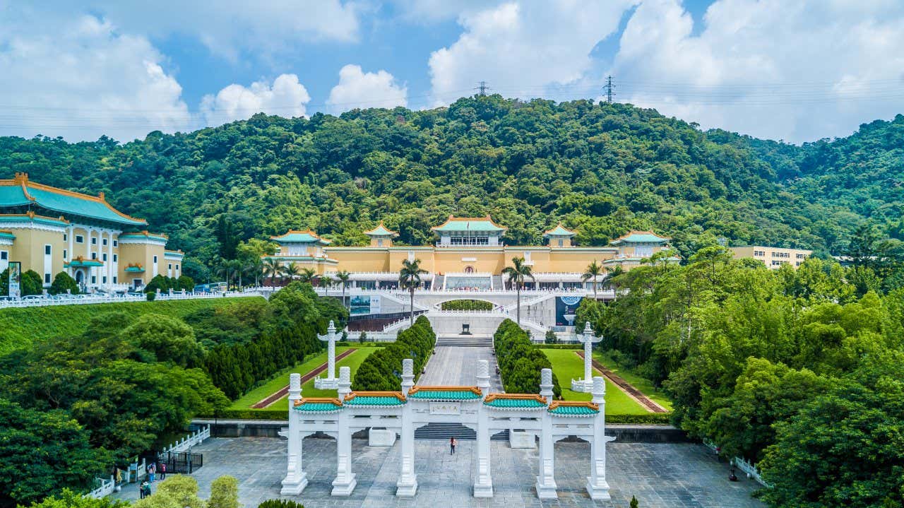 Giardini in stile cinese. con una grande corte in pietra circondata da aree verdi. Sul fondo un enorme edificio dai tetti turchesi.