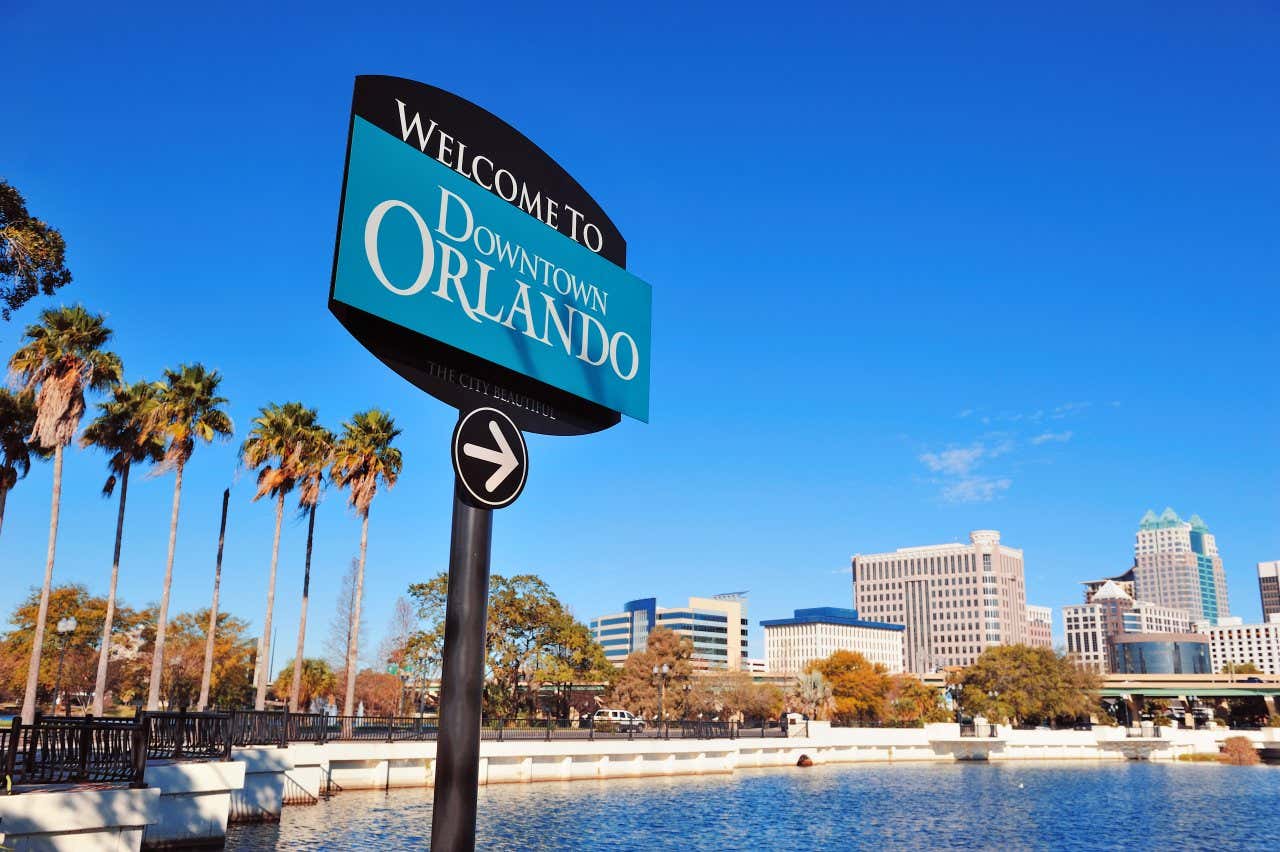 A blue and black sign saying "welcome to downtown orlando" pointing towards skyscrapers.