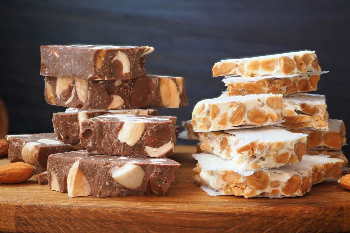 Dos tipos de turrones de almendra, uno de ellos con chocolate, dispuestos en tacos sobre una tabla de madera