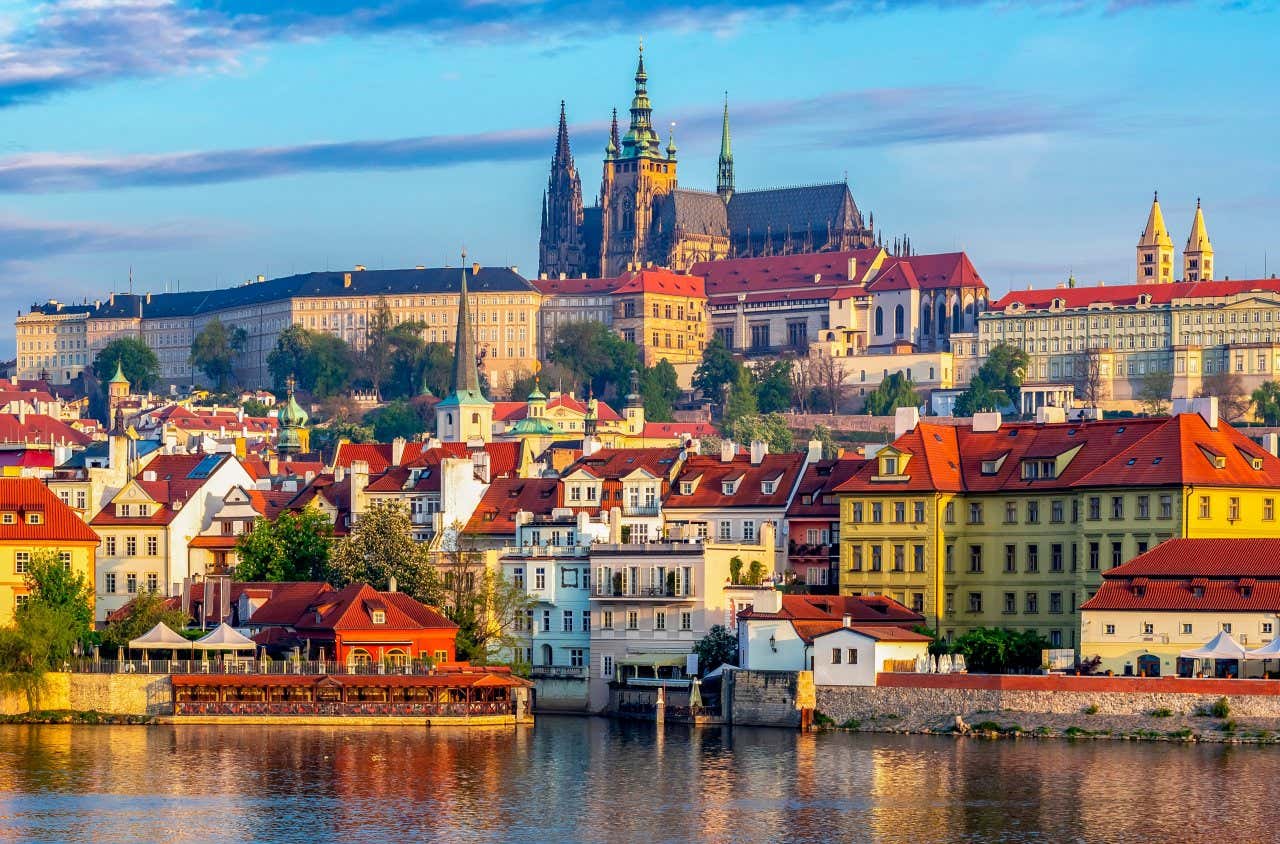 Una foto di Praga vista dal fiume, con case colorate e il castello in alto, illuminata dalla luce del tramonto