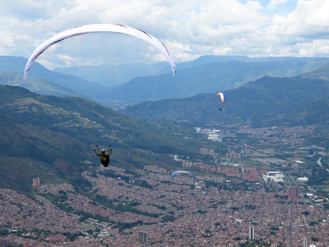 3 paragliders gliding above the city in Medellín Colombia, with jungle views in the background.
