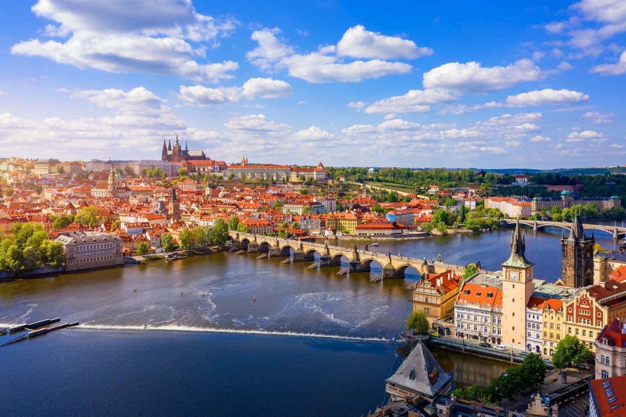 Vista panorâmica de Praga com uma ponte sobre o rio no centro e várias construções de tijolos típicos