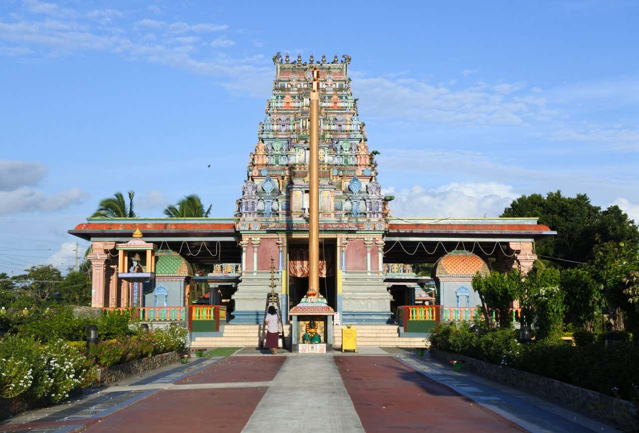 Sri Siva Subramaniya Temple under a blue sky with a woman walking outside it.