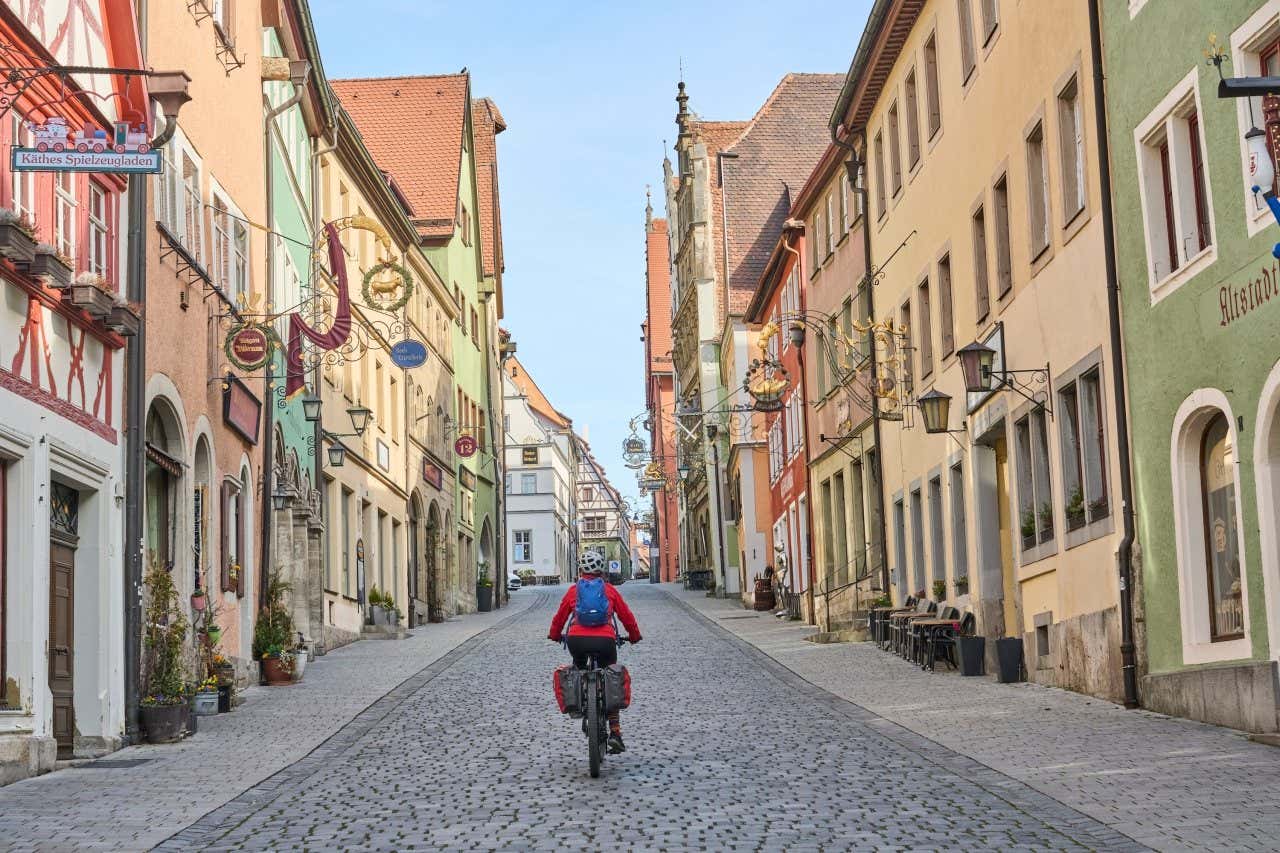 Mulher em um passeio de bicicleta no centro de Rotemburgo passando por ruas de paralelepípedos e construções históricas