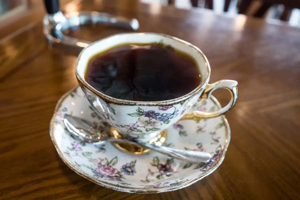 Uma xícara de porcelana vitoriana com um pires do mesmo estilo e uma colher de café com o lendário café Geisha do Panamá