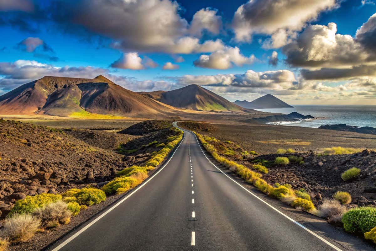 Una carretera sin coches acercándose a la costa y a varios conos volcánicos de la isla de Lanzarote