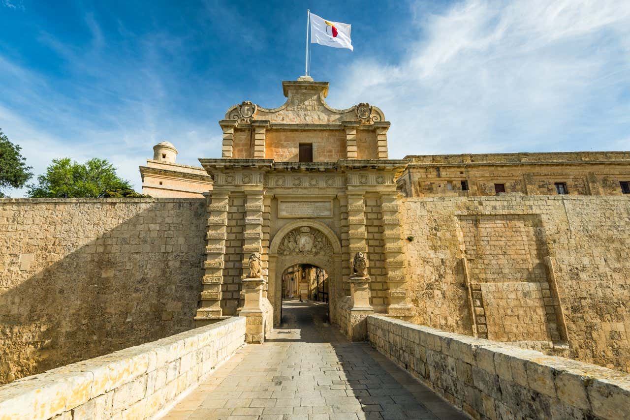 Un pont de pierre se terminant par une grande porte ornée, ouverte à l'intérieur des murs de Mdina