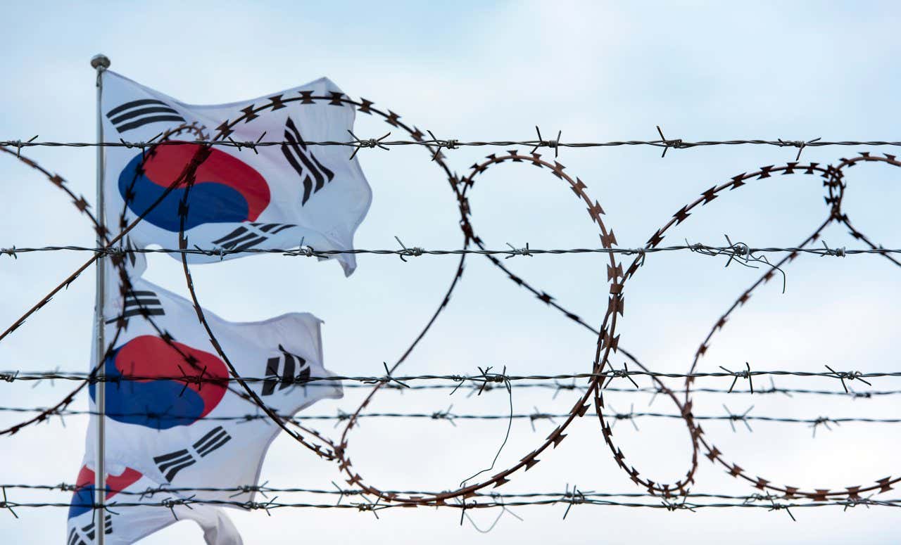 A barbed wire fence with the Republic of Korea flag in the background.