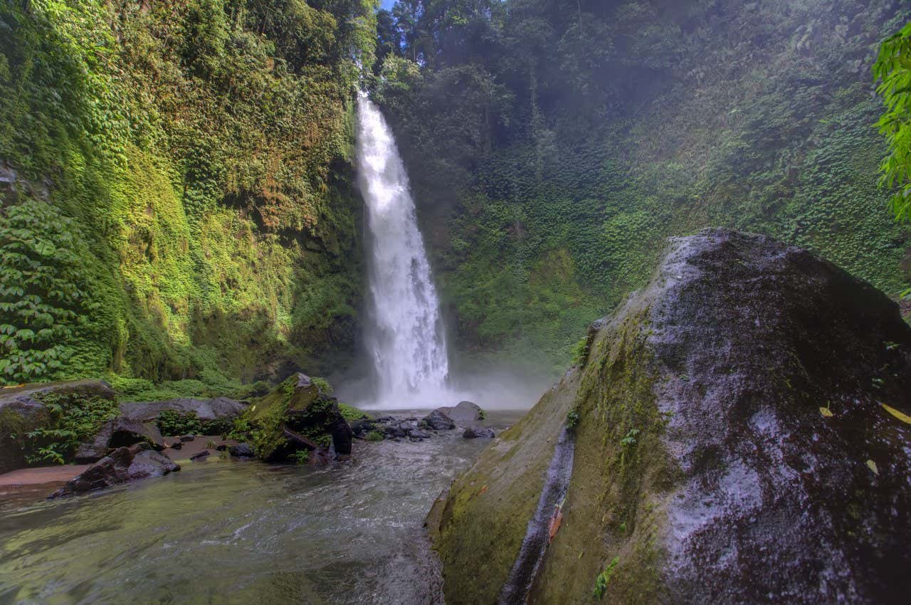 Nung Nung Waterfall, with a rock in the foreground and greenery all around the water.