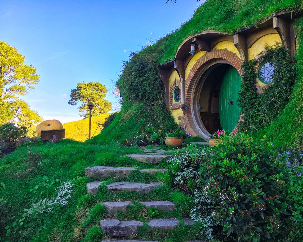 Una piccola porta tondeggiante di colore verde incastonata dentro una collina verde