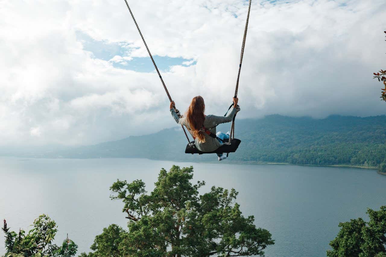 Una mujer columpiándose en un columpio de Bali, con una gran nube y una zona boscosa visibles al fondo