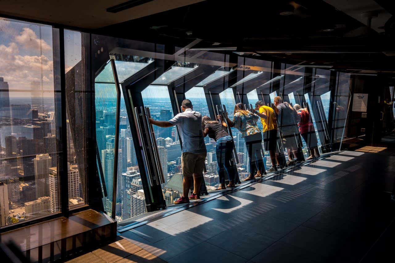 Uma fila de pessoas aproveita a atração 360 Chicago Observatory no edifício John Hancock, com vista para a cidade em um dia ensolarado