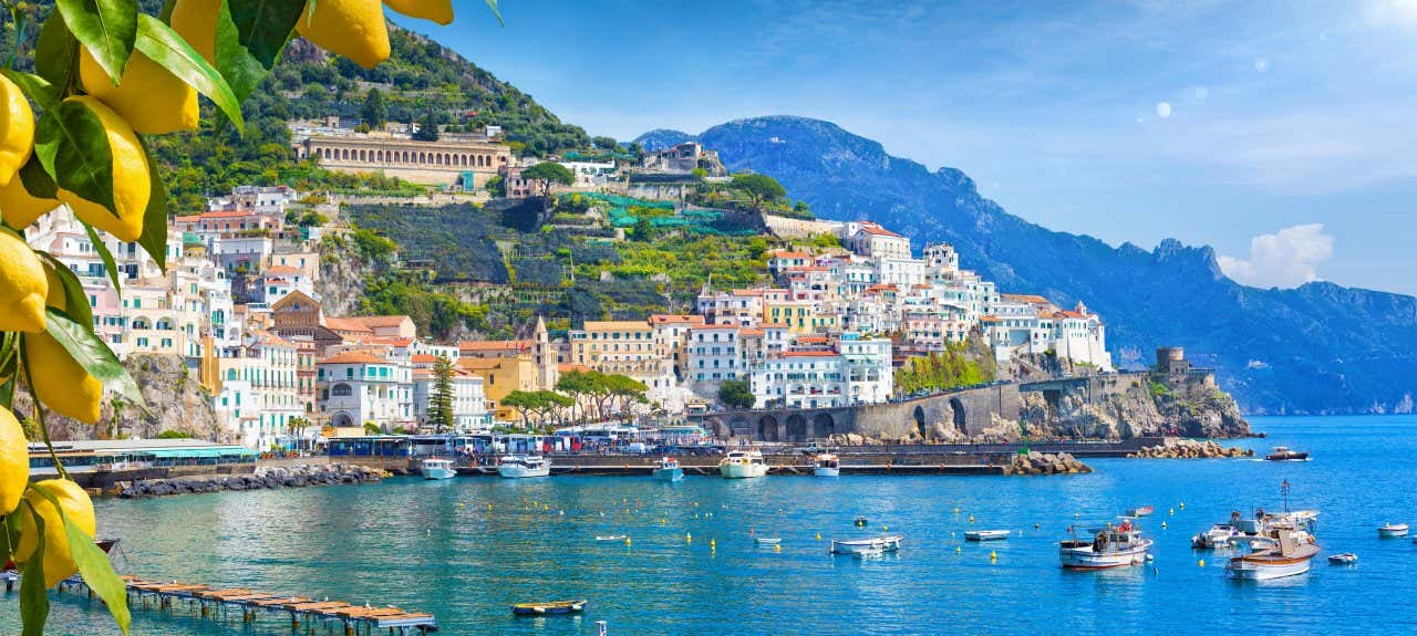 A view of houses in the Amalfi Coast with boats in the surrounding water under a blue sky.