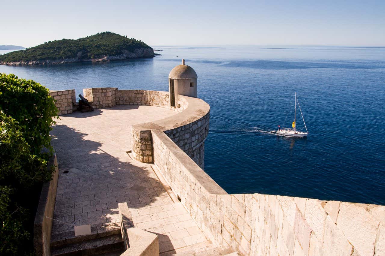 Balconata in cima alla torre di vedetta in pietra bianca affacciata sul mare con una barca e alcune isolette sullo sfondo in un giorno di sole