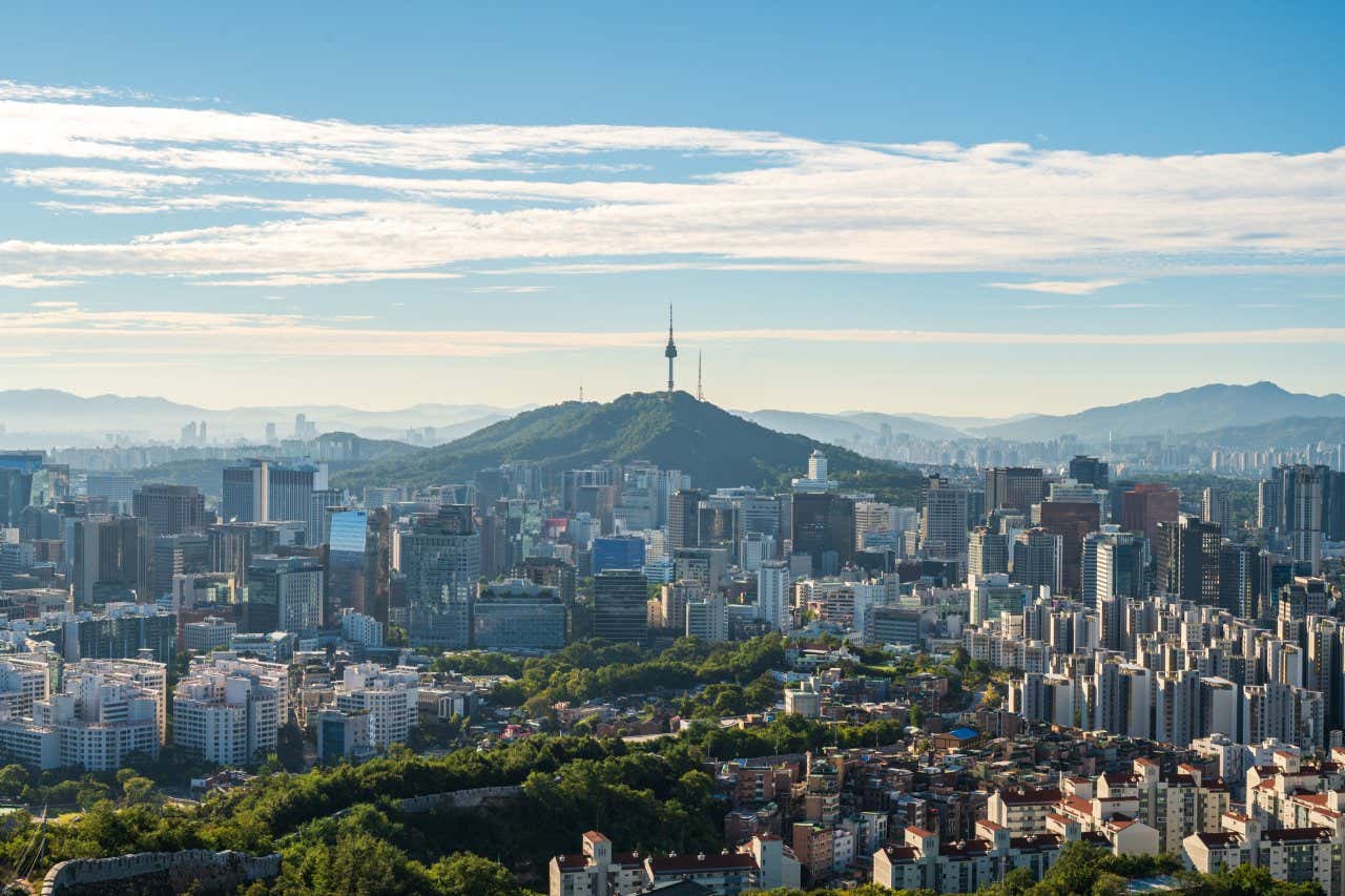 The N Seoul Tower as seen from afar, with a cloudy blue sky in the background.