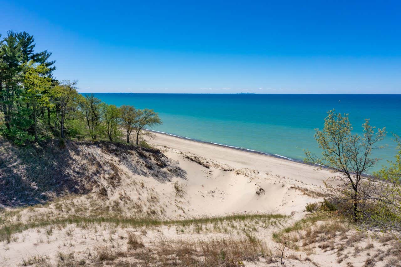 Vista panorâmica do Indiana Dunes National Park em um dia ensolarado, areia branca que leva a águas azul-turquesa e vegetação ao redor