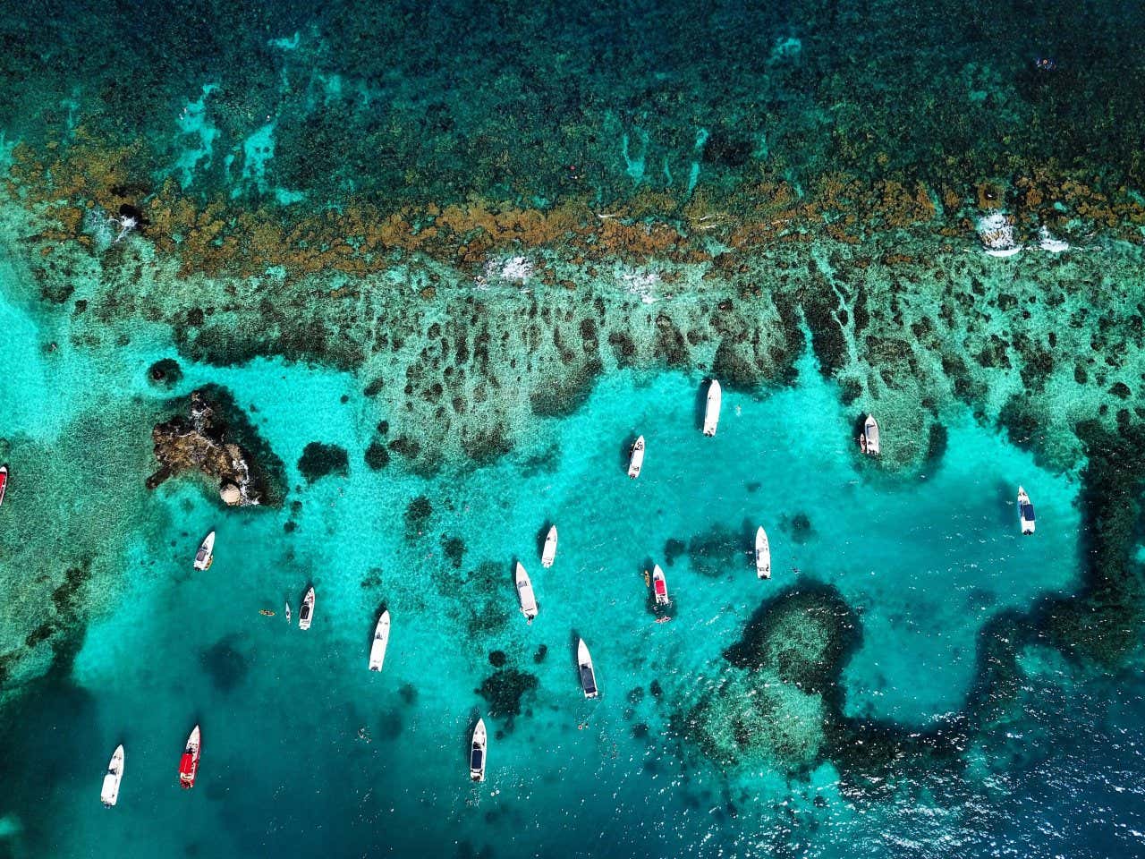 Vista aérea das ilhas do Rosário, com as águas turquesas e recifes de coral e muitos barcos