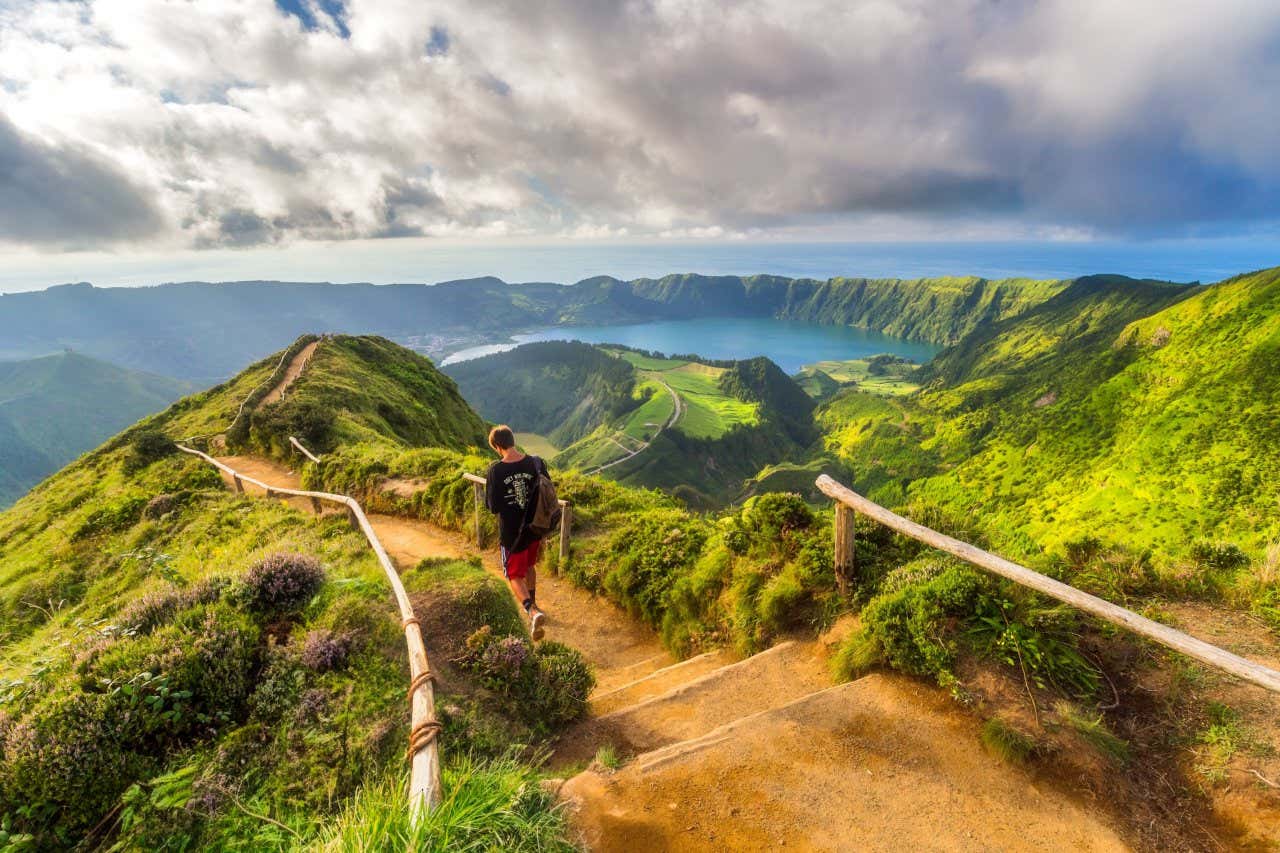 Uma pessoa fazendo trilha pelas paisagens de montanhas verdes e lagos  